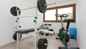 Une salle de sport équipée d’un banc de développé couché, d’un support à squats et d’un appareil elliptique.