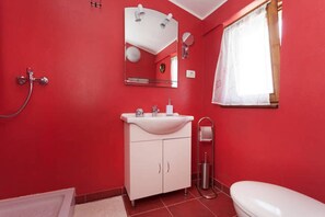 Un baño con paredes rojas, un lavabo blanco, un espejo, un inodoro y una ducha.