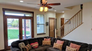 A living room with a sectional sofa, a ceiling fan, and a staircase leading to another level.