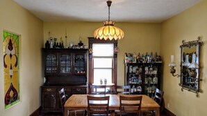 A dining room with a wooden table and chairs, a chandelier, a stained glass window, and a cabinet filled with bottles and glassware.
