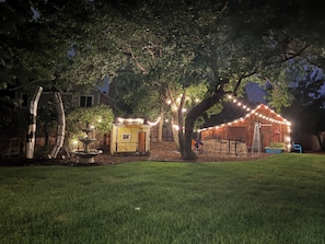 A rustic outdoor setting with a wooden structure, string lights, and a dining area.