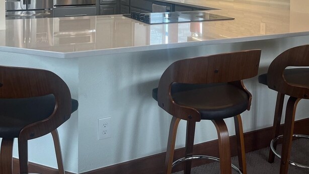 A modern kitchen with stainless steel appliances, a large island with bar stools, pendant lighting, and a view of the outdoors.