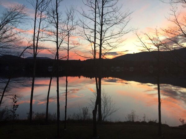 Une vue paisible sur un lac, avec des arbres sans feuilles et le reflet d’un coucher de soleil.