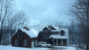 Un'ampia casa a due piani con tetto imbiancato dalla neve e vialetto, circondata da alberi.