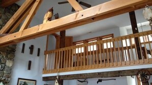 Un interno rustico con travi a vista in legno, una parete in pietra e un balcone con ringhiera in legno.