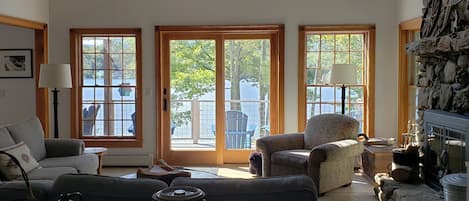 A spacious living room with a high ceiling, large windows, a stone fireplace, and a cozy seating area.