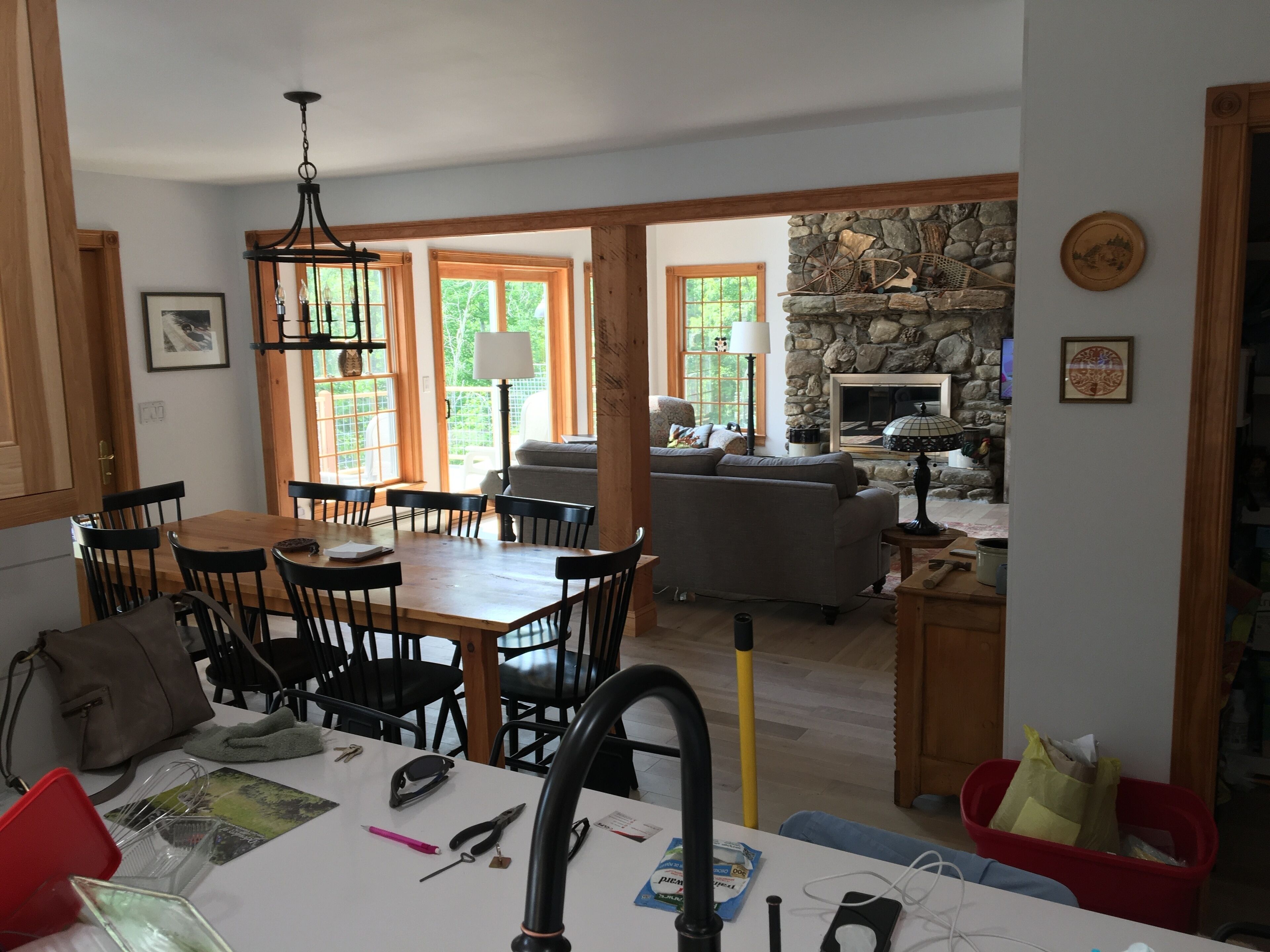 A dining area with a wooden table and chairs, a kitchen area with a sink and utensils, and a living room with a stone fireplace.