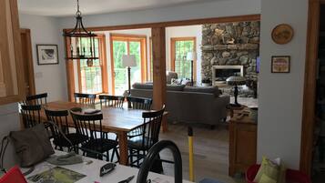 A dining area with a wooden table and chairs, a kitchen area with a sink and utensils, and a living room with a stone fireplace.