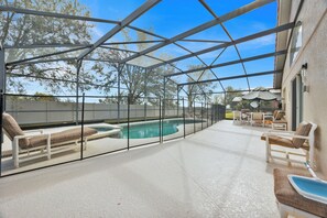 A covered outdoor area with a pool, lounge chairs, and umbrellas. - Villa Florida Belle - Solana Resort - Luxury Orlando Villa close to Disney (Davenport)