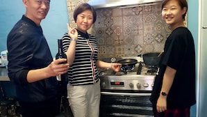 Una cocina con estufa, una persona sosteniendo una botella y otra persona sosteniendo una sartén.