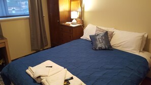 Quarto de hotel com cama, mesa de cabeceira, abajur e janela com cortinas.