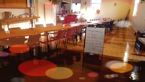Un amplio comedor con varias mesas y sillas, una cocina al fondo y un cartel que detalla las opciones de comida y las normas.