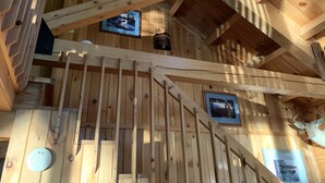 Een houten interieur met een trap, houten balken en foto's in lijsten aan de wanden.