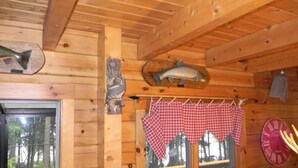 Interieur van een houten hutje met een raam, houten plafond en geruit tafelkleed dat over een deuropening hangt.