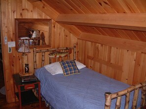 A wooden room with a bed, a nightstand, a lamp, and a mirror. - Log home on untouched cold stream lake (Lowell)