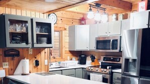 Een keuken met houten wanden, witte kasten, een centraal eiland met barstoelen, roestvrijstalen apparatuur en hanglampen.