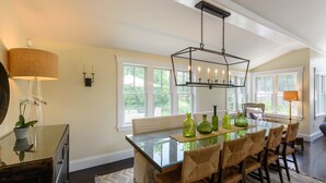 A dining area with a glass table, wicker chairs, and a hanging light fixture. - Katama Luxury - 5+ BR home w/ Heated Pool near the Field Club (Edgartown)