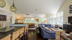 A spacious living area with a large sofa, a dining table, and a kitchen area with a bar. - Katama Luxury - 5+ BR home w/ Heated Pool near the Field Club (Edgartown)