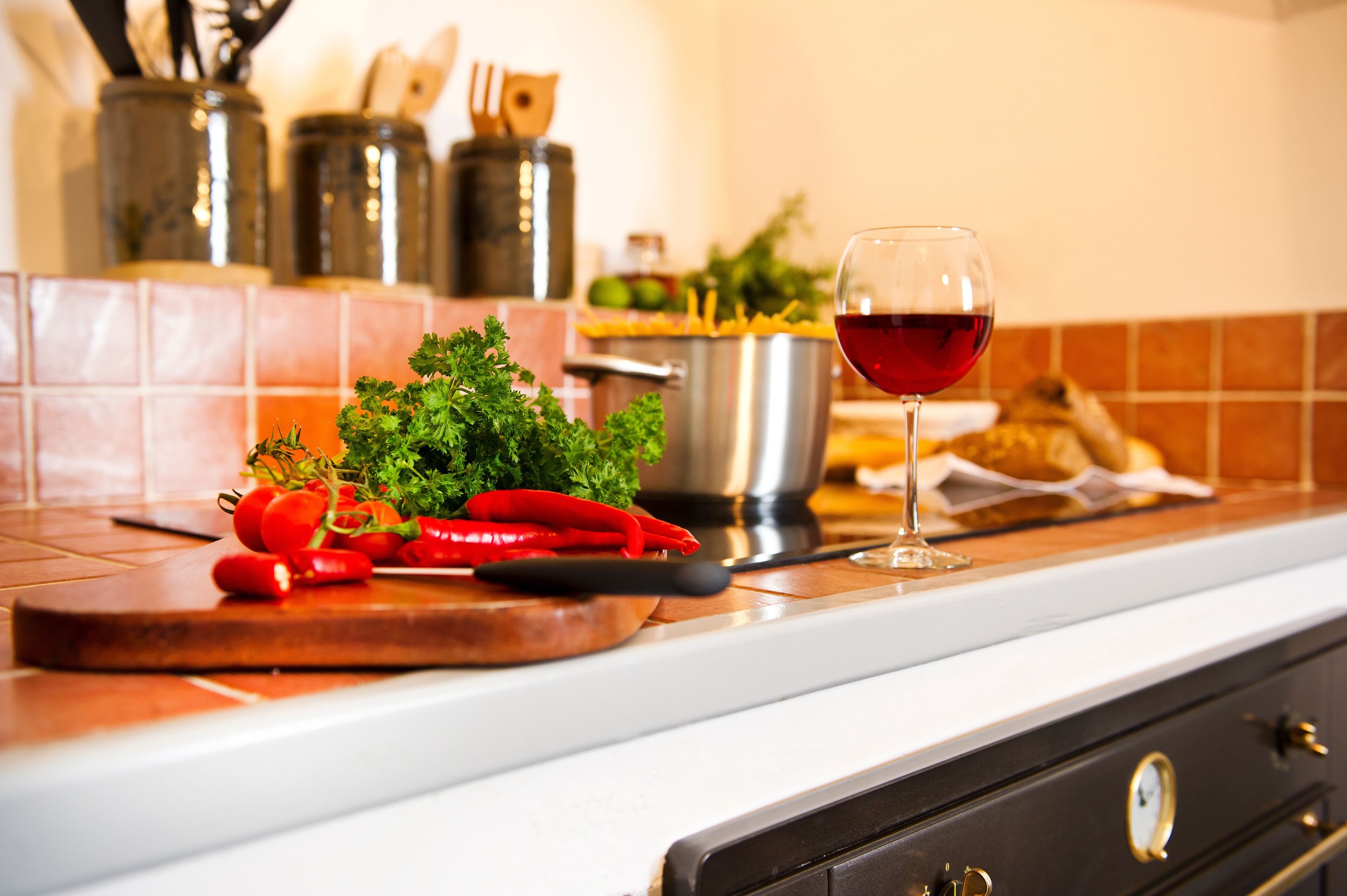 A kitchen counter with fresh vegetables, a glass of red wine, and cooking utensils.