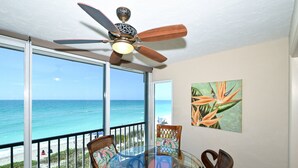 A balcony with a glass table and chairs, a ceiling fan, and a view of the ocean.