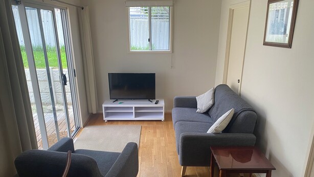 A living room with a grey sofa, a wooden coffee table, a flat-screen TV on a white stand, and a sliding glass door leading to an outdoor area. - North Perth Cottage - Close to city (North Perth)
