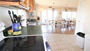A kitchen with a stove, sink, and cabinets. There is a dining area with chairs and a table. - Watch the Sunset from this Bayfront Home! (1349) (Wellfleet)