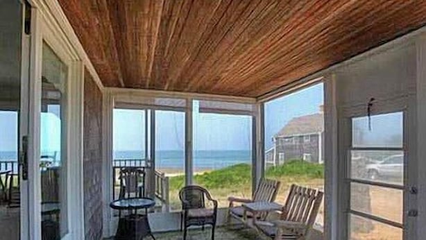 A covered outdoor seating area with a view of the ocean and a house in the background. - Watch the Sunset from this Bayfront Home! (1349) (Wellfleet)