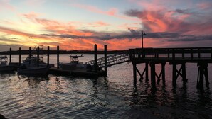 Un muelle con barcos, un espigón y un atardecer sobre el agua.