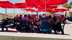 Un área de comedor frente a la playa, con sombrillas rojas y sillas negras.