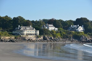 A beachfront property with multiple large houses, a sandy beach, and a rocky shoreline.