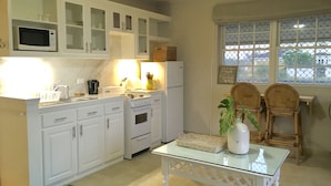 A kitchen with white cabinets, a microwave, a stove, and a refrigerator. There is a glass table with a vase and a basket. -  Spacious Oceanview One Bedroom Apartment (Atlantic Shores)