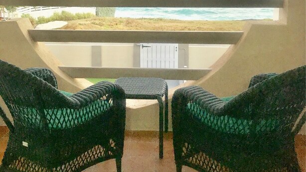 A balcony with two wicker chairs and a small table, overlooking a beach and ocean with a sunset view. -  Spacious Oceanview One Bedroom Apartment (Atlantic Shores)