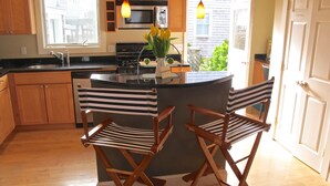 A kitchen with wooden cabinets, a black countertop, a microwave, a stove, and two striped chairs.