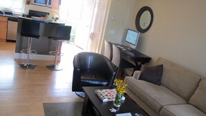 A modern living room with a sofa, a coffee table with a vase of flowers, a dining area with a bar stool, and a kitchen with a microwave.