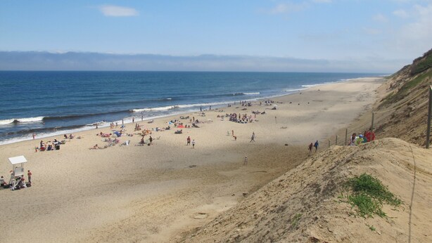 A beach with people, umbrellas, and a lifeguard tower.