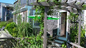 A wooden pergola with climbing plants, a stone bench, and a door leading to a porch.