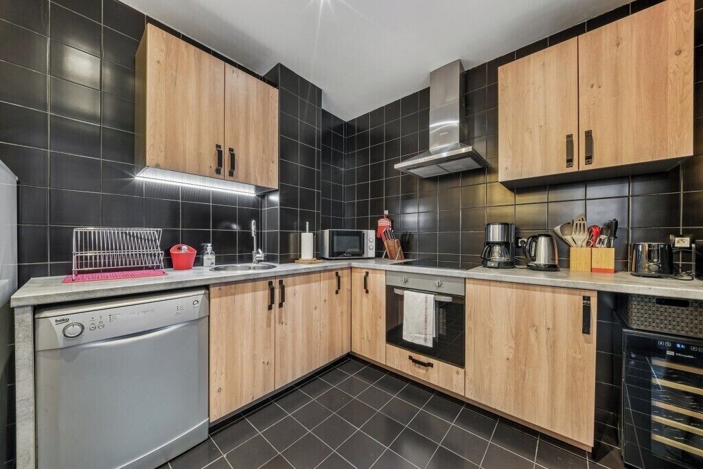 A modern kitchen with black tiles, wooden cabinets, a dishwasher, a microwave, and a coffee maker.