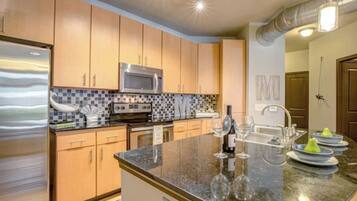A modern kitchen with wooden cabinets, a stainless steel refrigerator, a microwave, and a granite countertop.