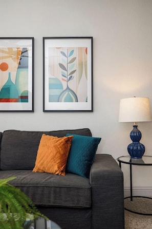 A modern living room with a grey sofa, two cushions, a blue lamp, and abstract art on the wall.