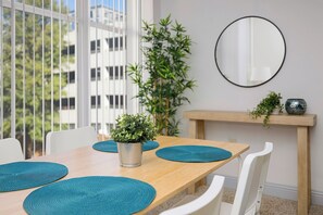 A dining area with a wooden table, white chairs, and teal placemats. A potted plant is on the table, and a mirror hangs on the wall.