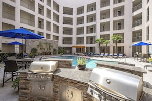 An outdoor pool area with a barbecue station, lounge chairs, and umbrellas.