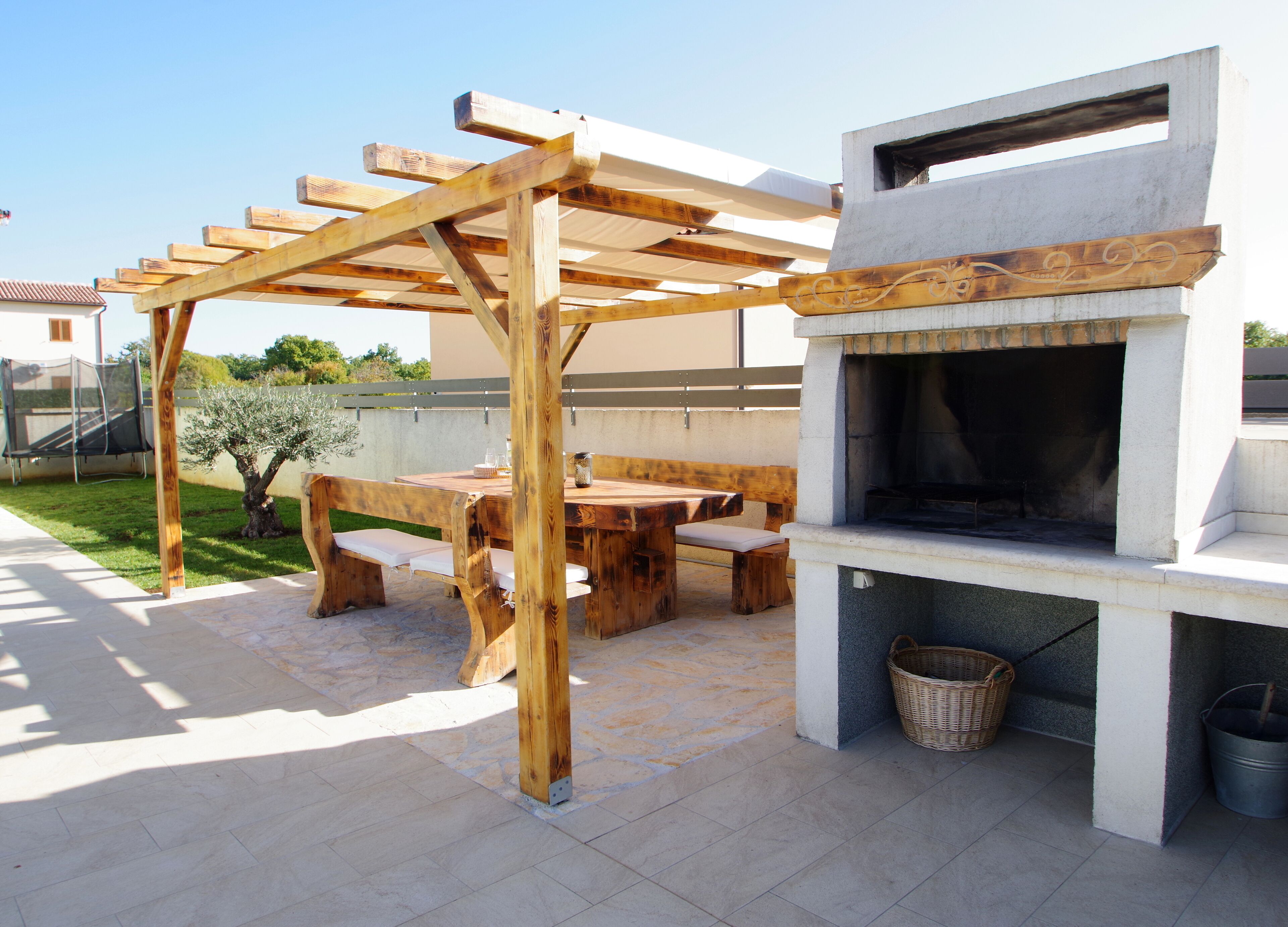 An outdoor patio with a wooden pergola, a stone-tiled floor, and a built-in barbecue grill.
