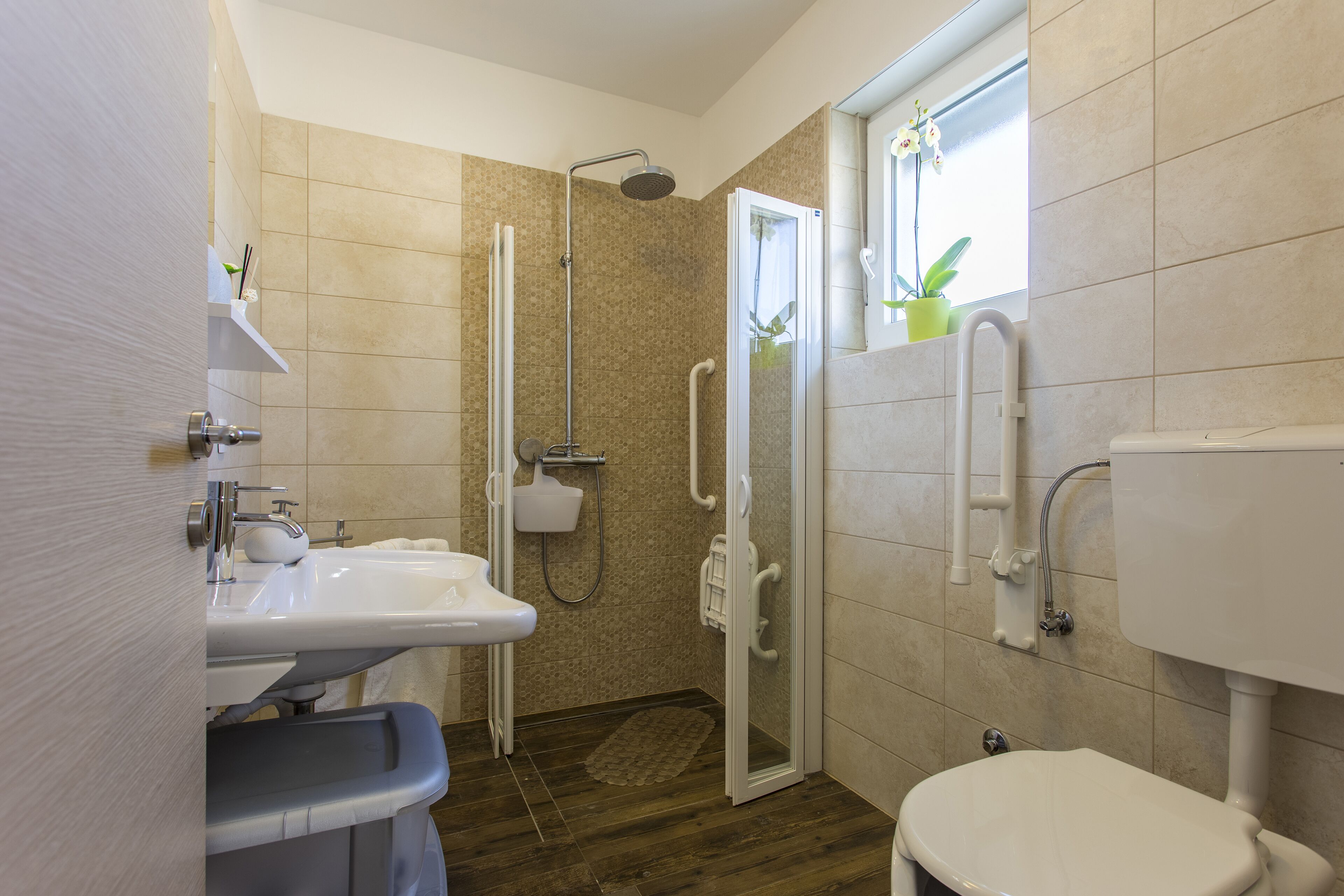 Een badkamer met douche, toilet, wastafel en een raam met een plant.