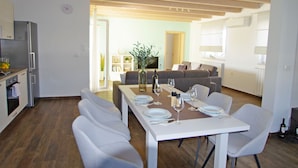 Une cuisine moderne avec des armoires blanches, un four encastré et un réfrigérateur. On y trouve un coin repas avec une table blanche dressée pour quatre personnes, entourée de chaises blanches.