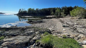 A rocky shoreline with clear water, trees, and a bright sun.