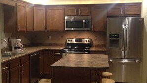 A kitchen with wooden cabinets, a stainless steel refrigerator, a microwave, and a stove.