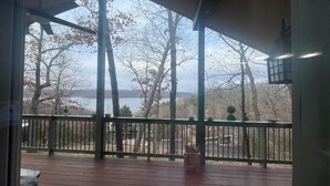 A wooden deck with a railing, a hanging lantern, and a view of trees and a body of water.
