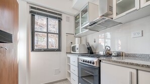 Eine moderne Küche mit weißen Schränken, einem Edelstahlherd, einer Mikrowelle und einem Fenster mit Jalousien.