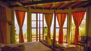 Una habitación con cama, una silla y ventanas grandes con cortinas.