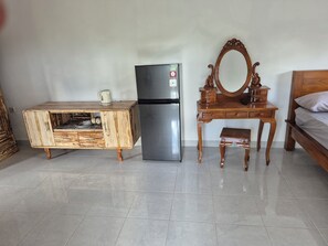 A bedroom with a bed, a wooden dresser, a mirror, a refrigerator, and a tiled floor.